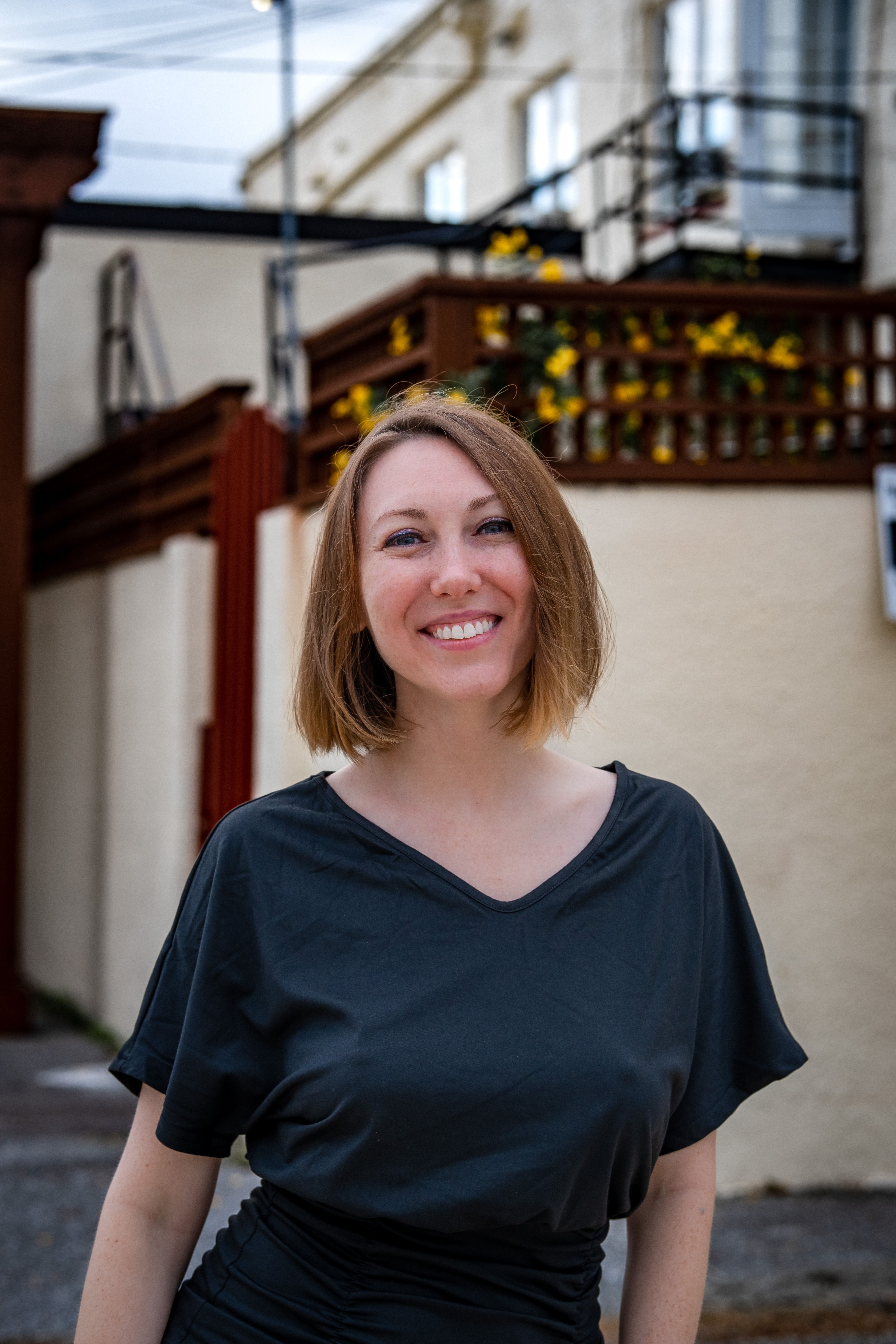 Relaxed client portrait outdoors near a building with flowering balcony railings in a calm urban setting